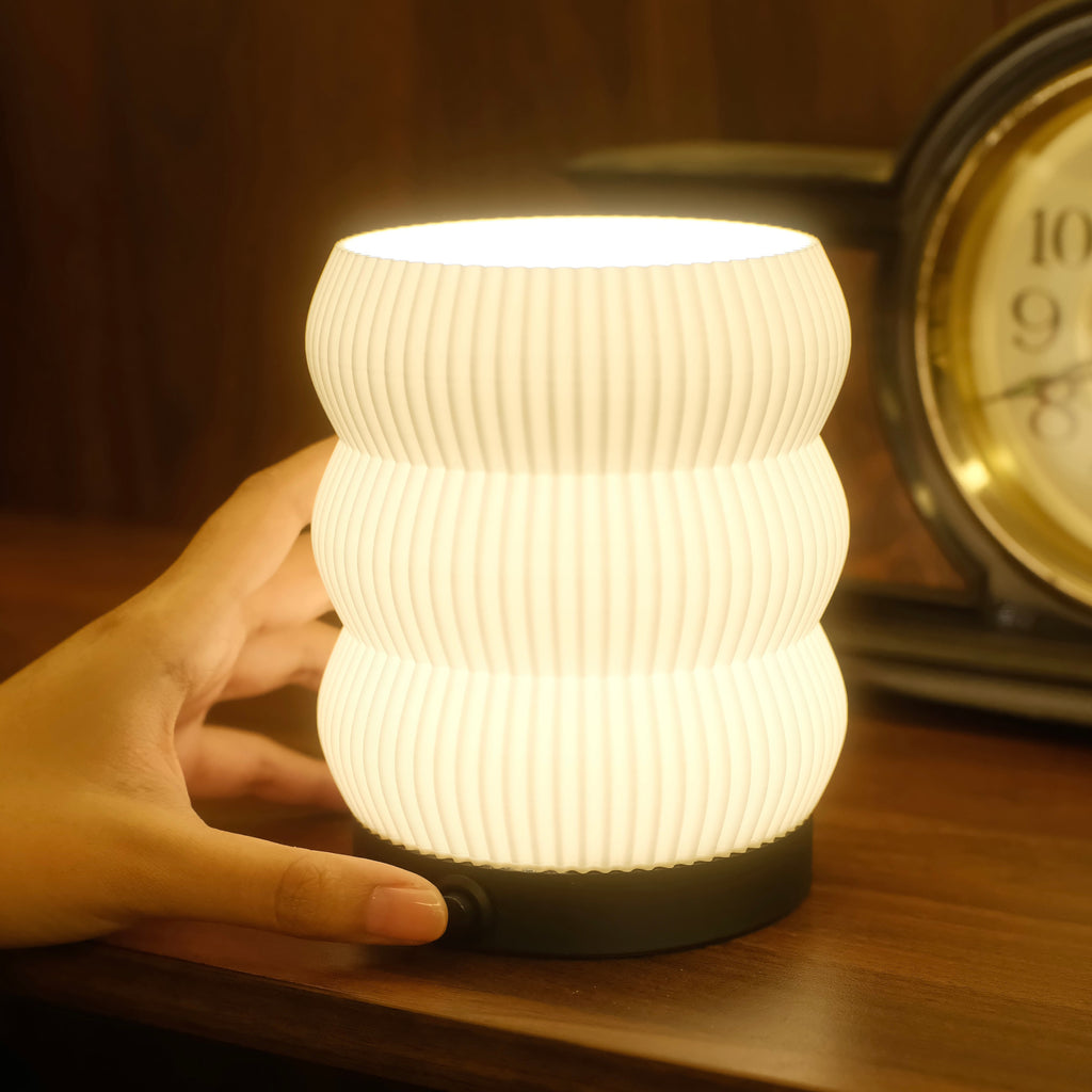 Hand holding a textured night light on a wooden surface with an alarm clock in the background.