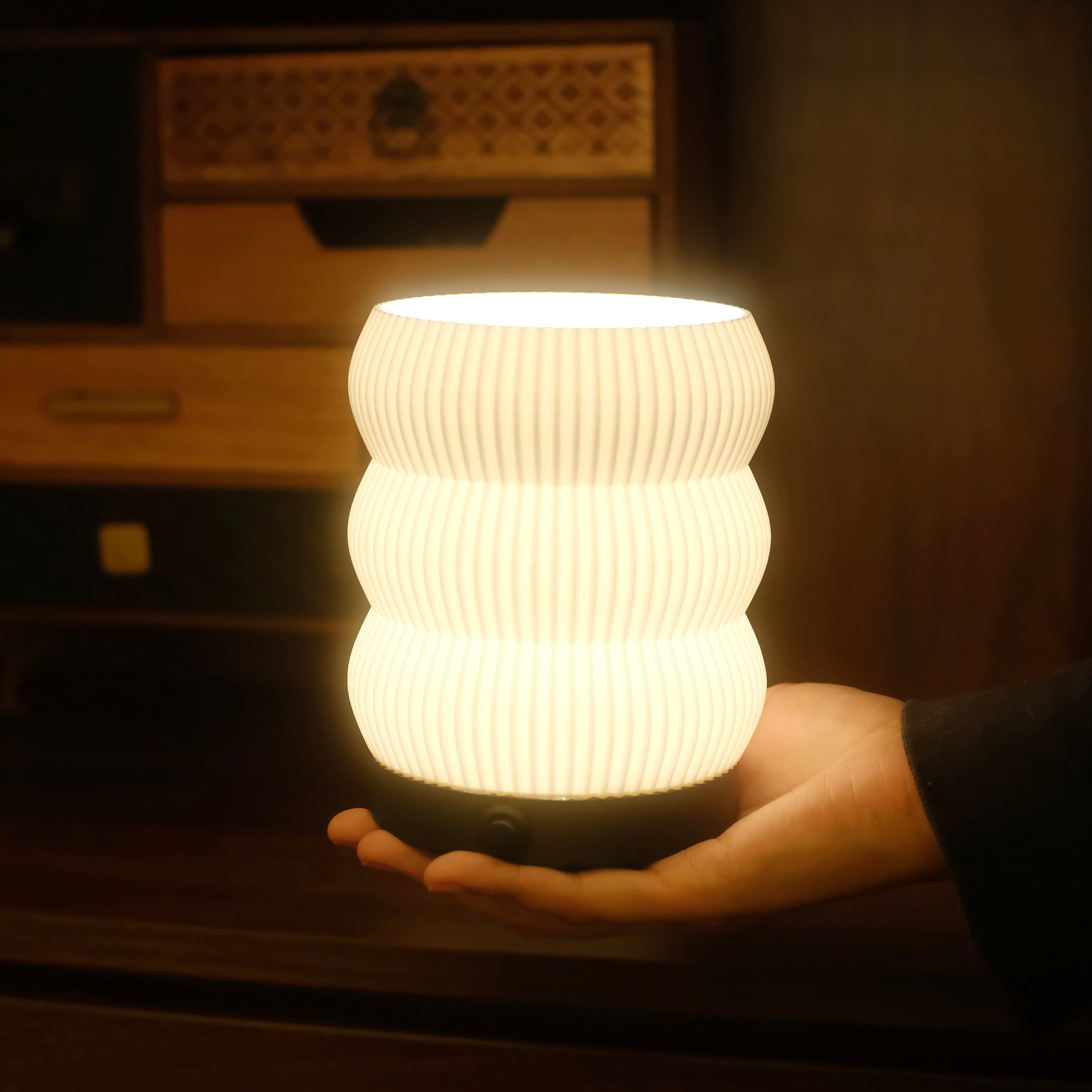 Hand holding a glowing white textured lamp against a dark background